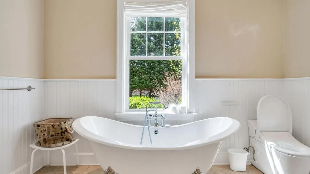 Un baño con una bañera independiente bajo una ventana.