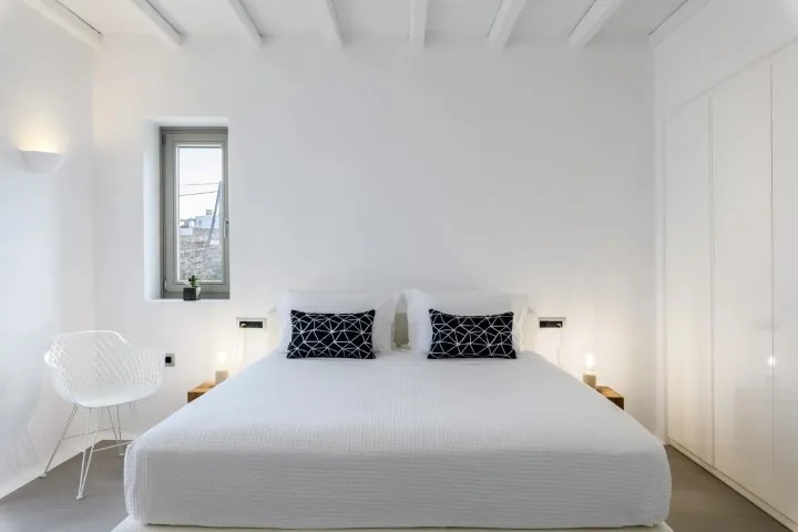 A bright bedroom with a bed beneath a white beamed ceiling.