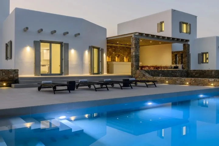 A modern villa faces a swimming pool, with lounge seating on the patio.