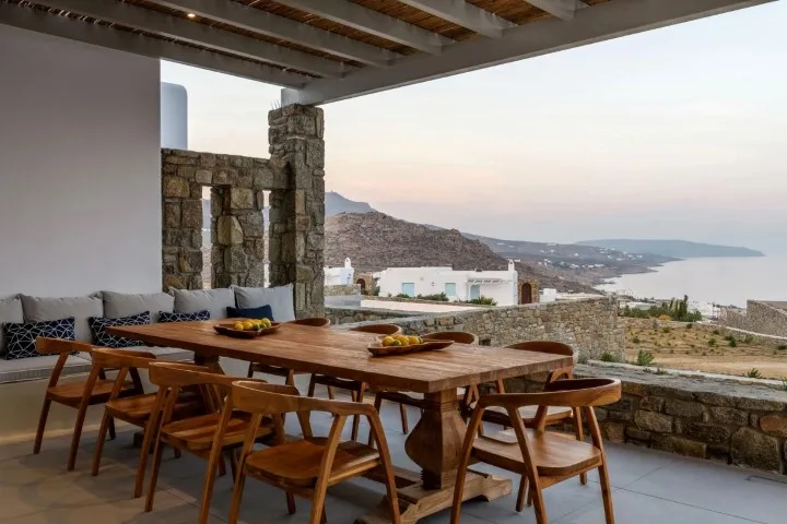 A covered outdoor dining area with a wooden table overlooking the sea.