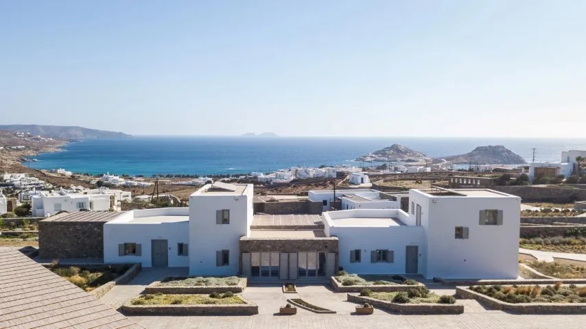 A modern white villa overlooks the sea and surrounding coastal landscape.