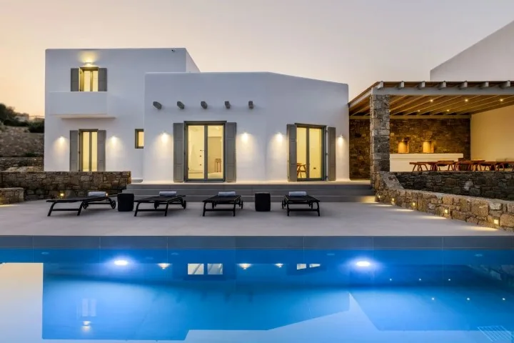 A modern villa facade overlooks a swimming pool and outdoor seating.
