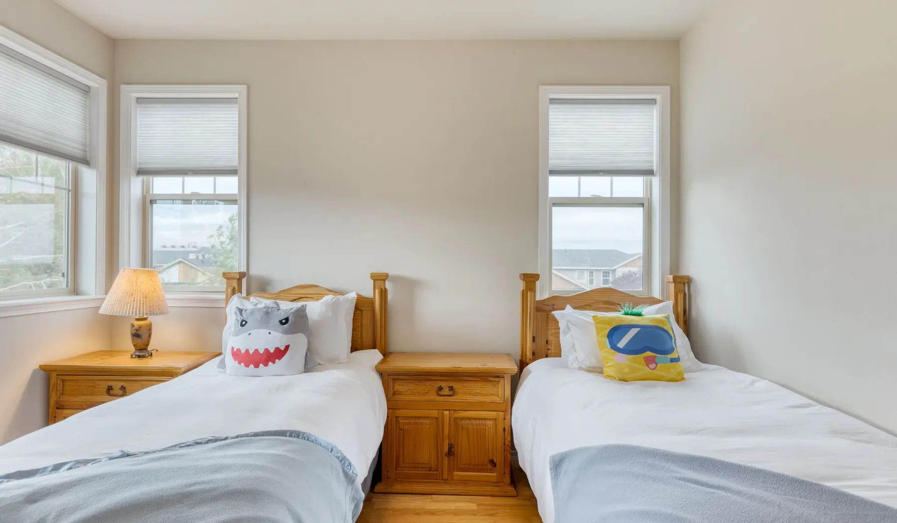 A bedroom with two single beds, wooden nightstands, and windows.