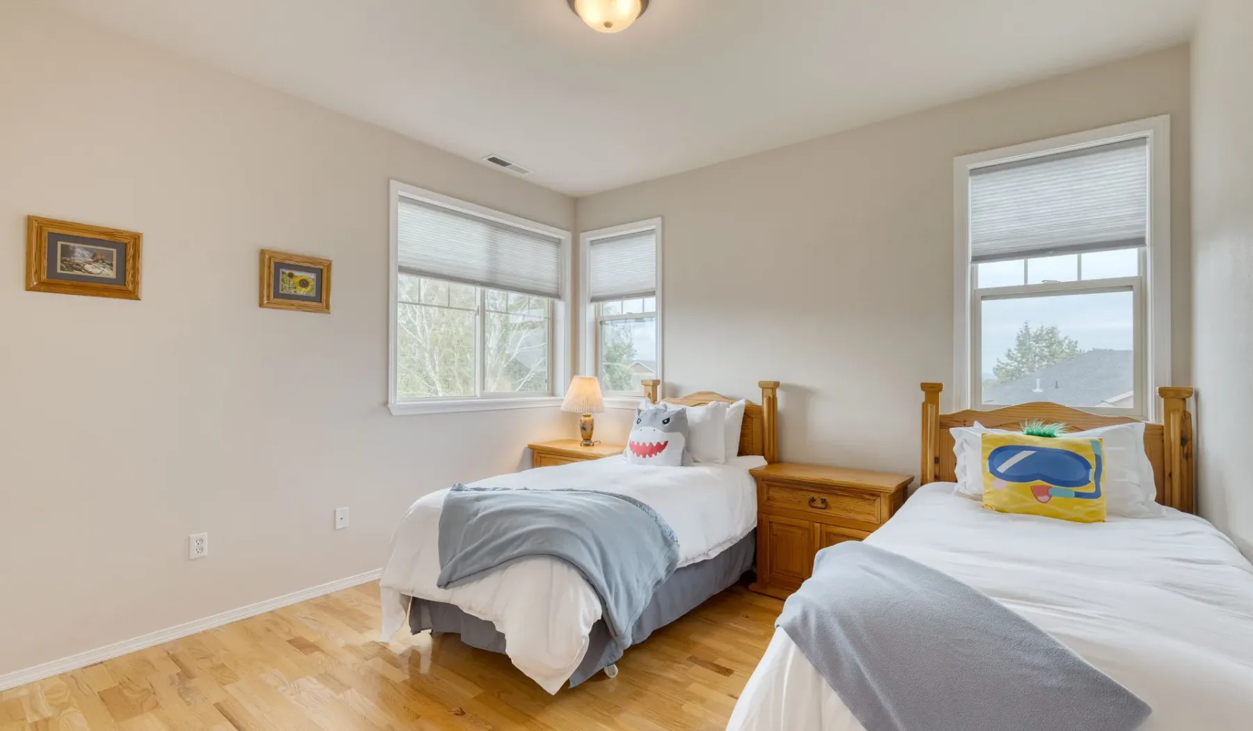 A bright bedroom with two beds and windows along the corner.