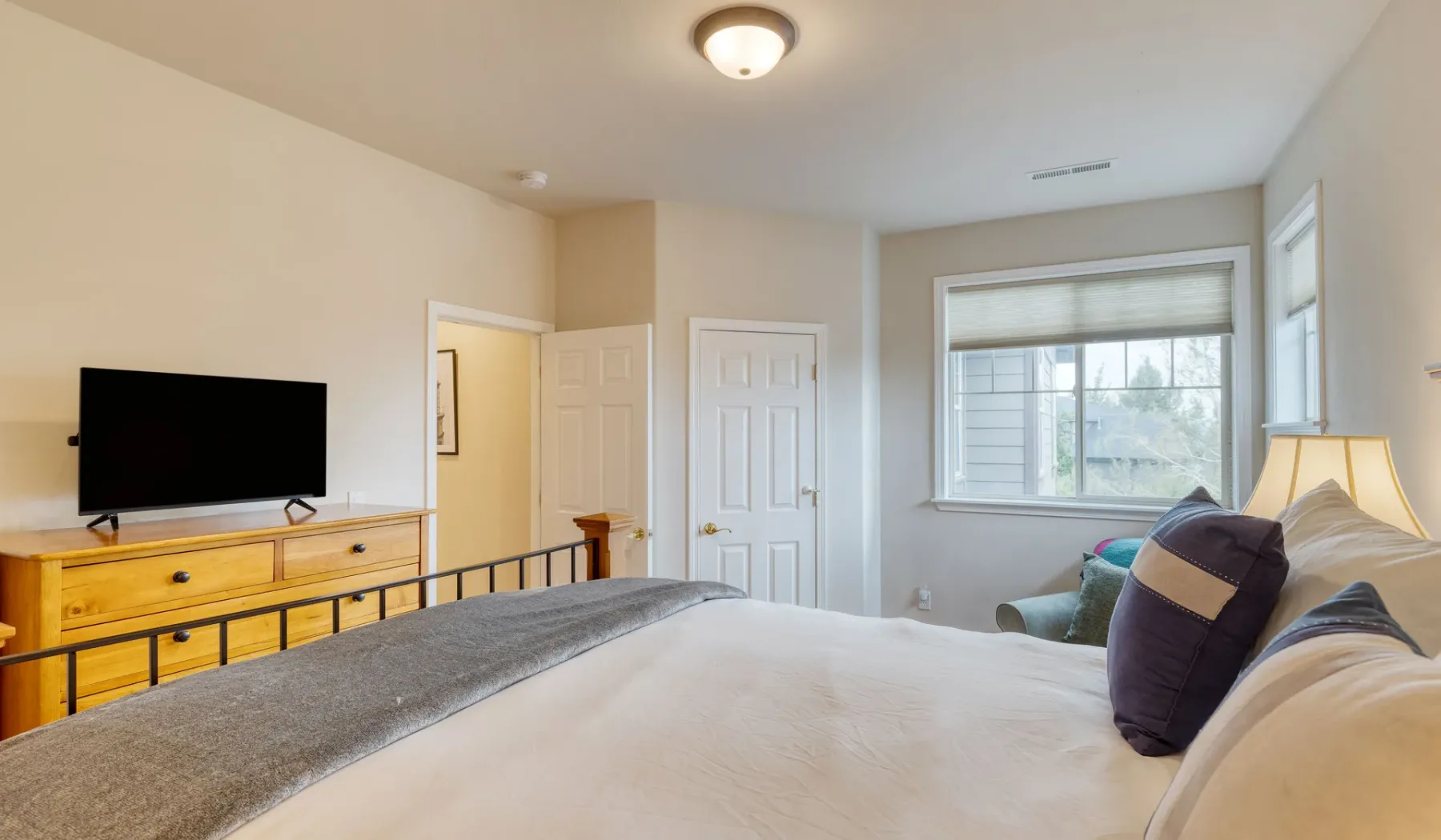 Bedroom with a large bed, dresser, and television beside a window.