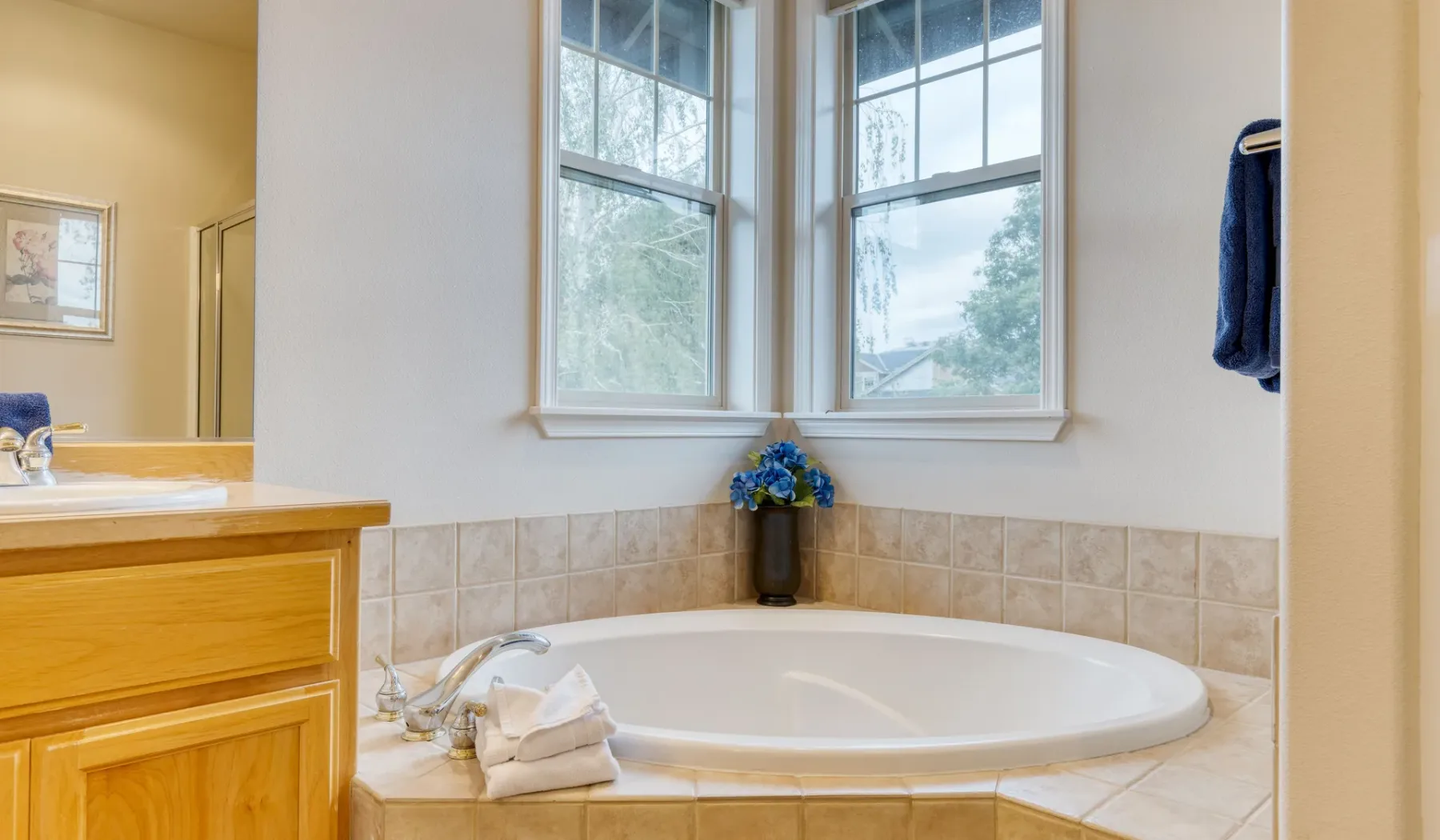 A bathroom with a large corner bathtub beneath two windows.