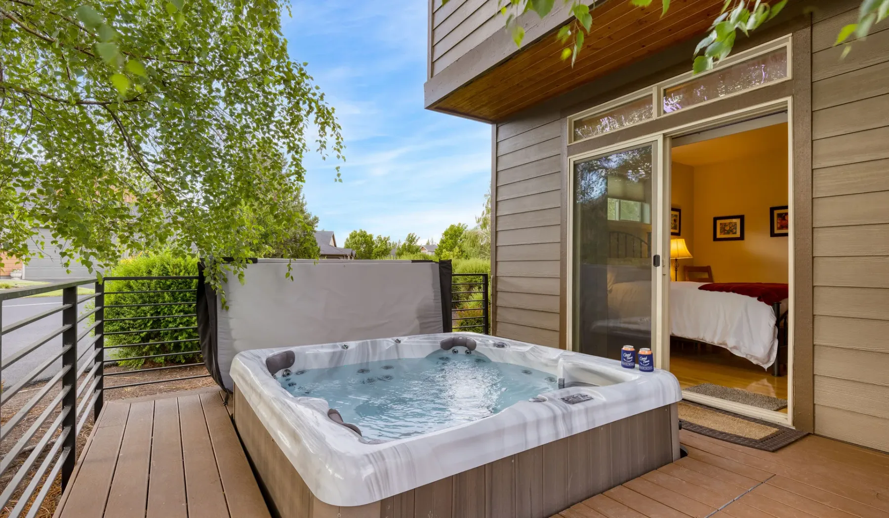 An outdoor hot tub sits on a wooden deck beside an open bedroom doorway.