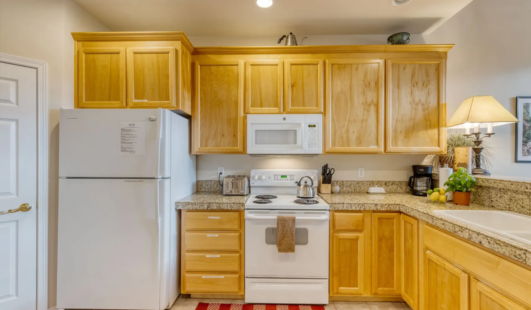 A bright kitchen with wooden cabinets, a refrigerator, and an electric range.