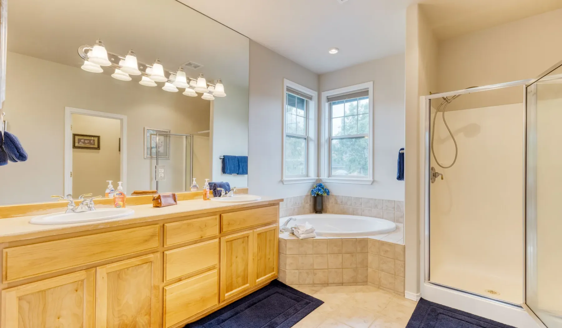 A bright bathroom with a long vanity, bathtub, and glass-enclosed shower.