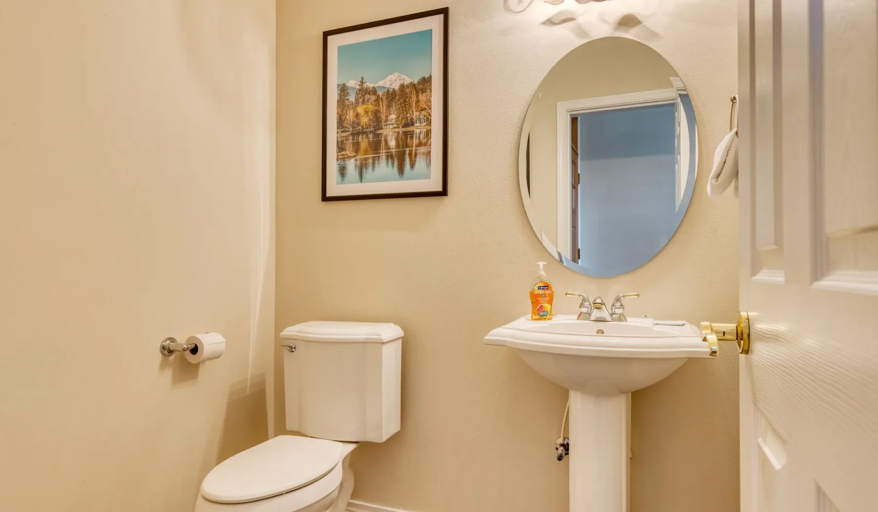 A bathroom with a toilet, pedestal sink, and round mirror.