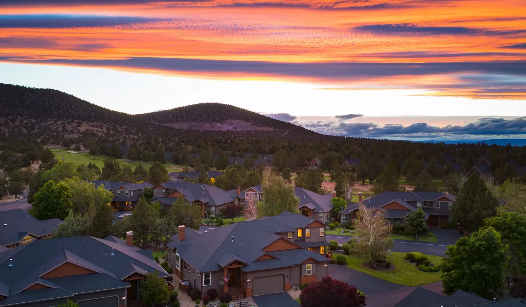 A residential neighborhood sits beneath hills and a colorful sunset sky.