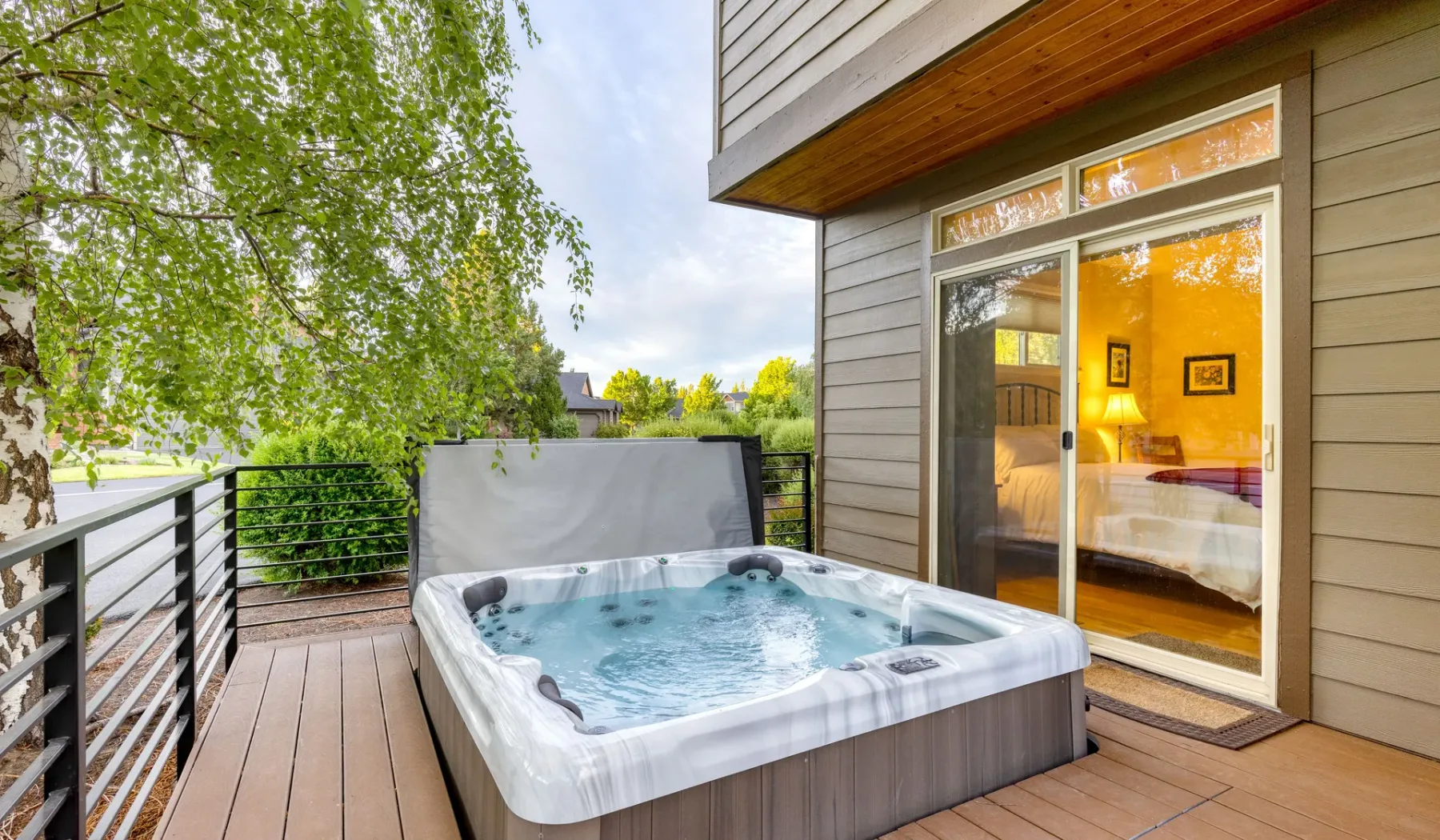 An outdoor hot tub sits on a wooden deck beside a glass door.