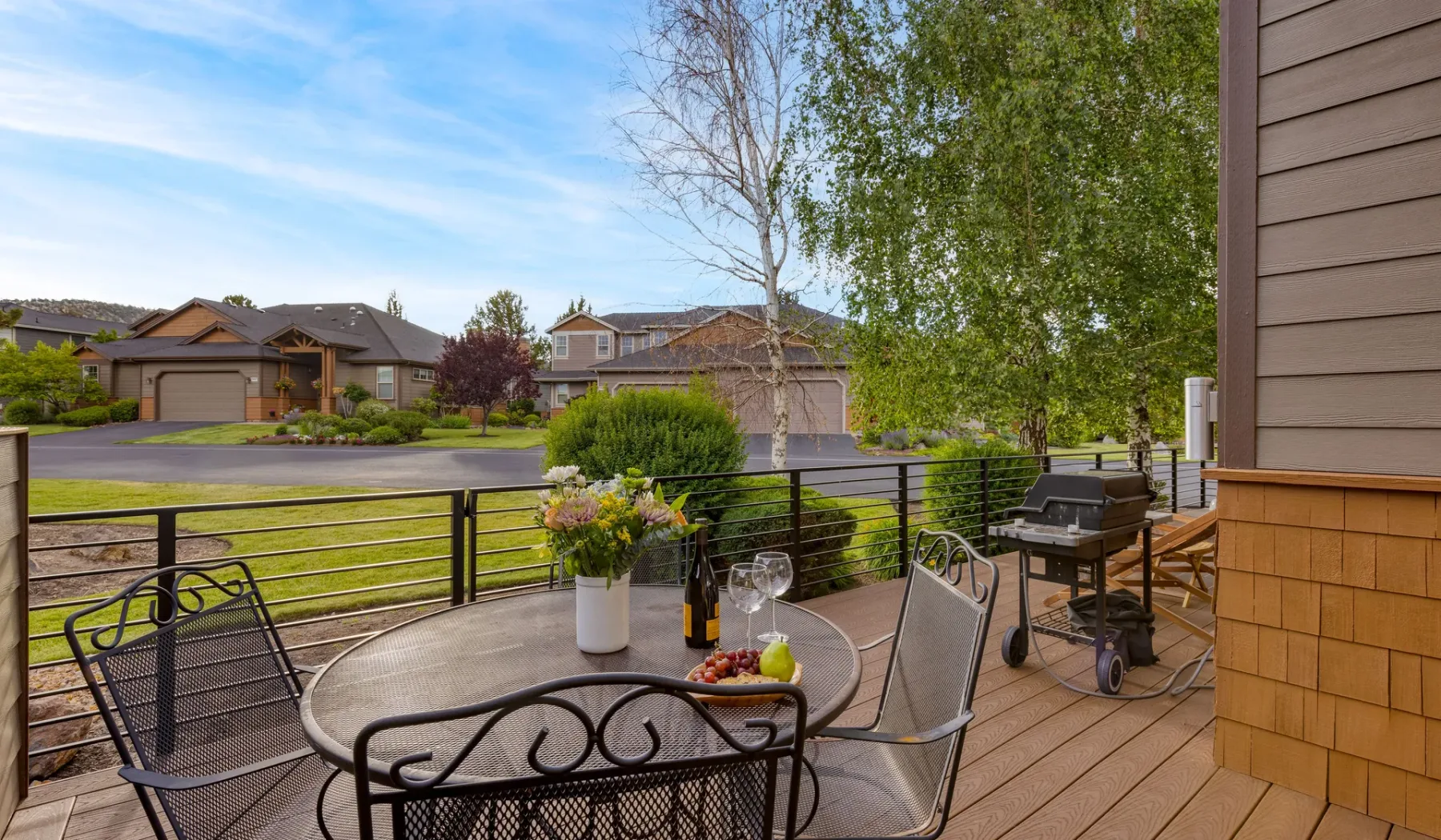 A wooden deck overlooks a residential street, with a table and seating.