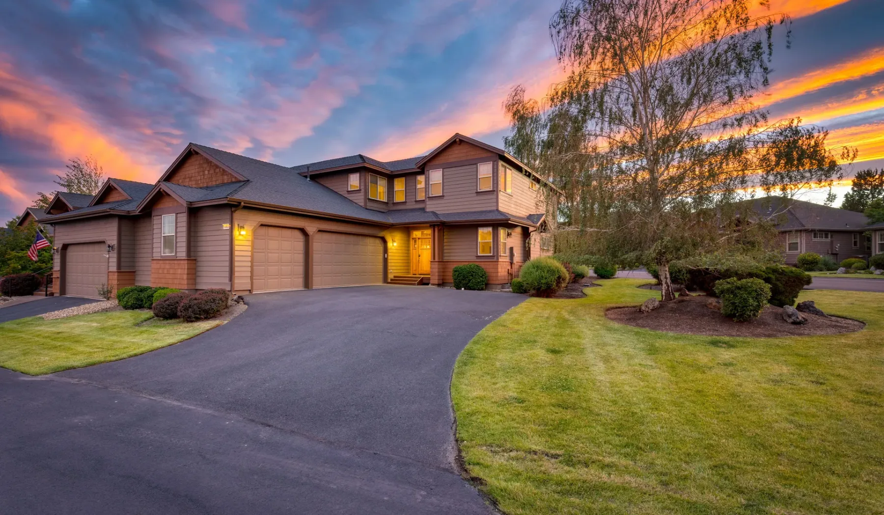 A large house with a paved driveway and lawn beneath a colorful sunset sky.