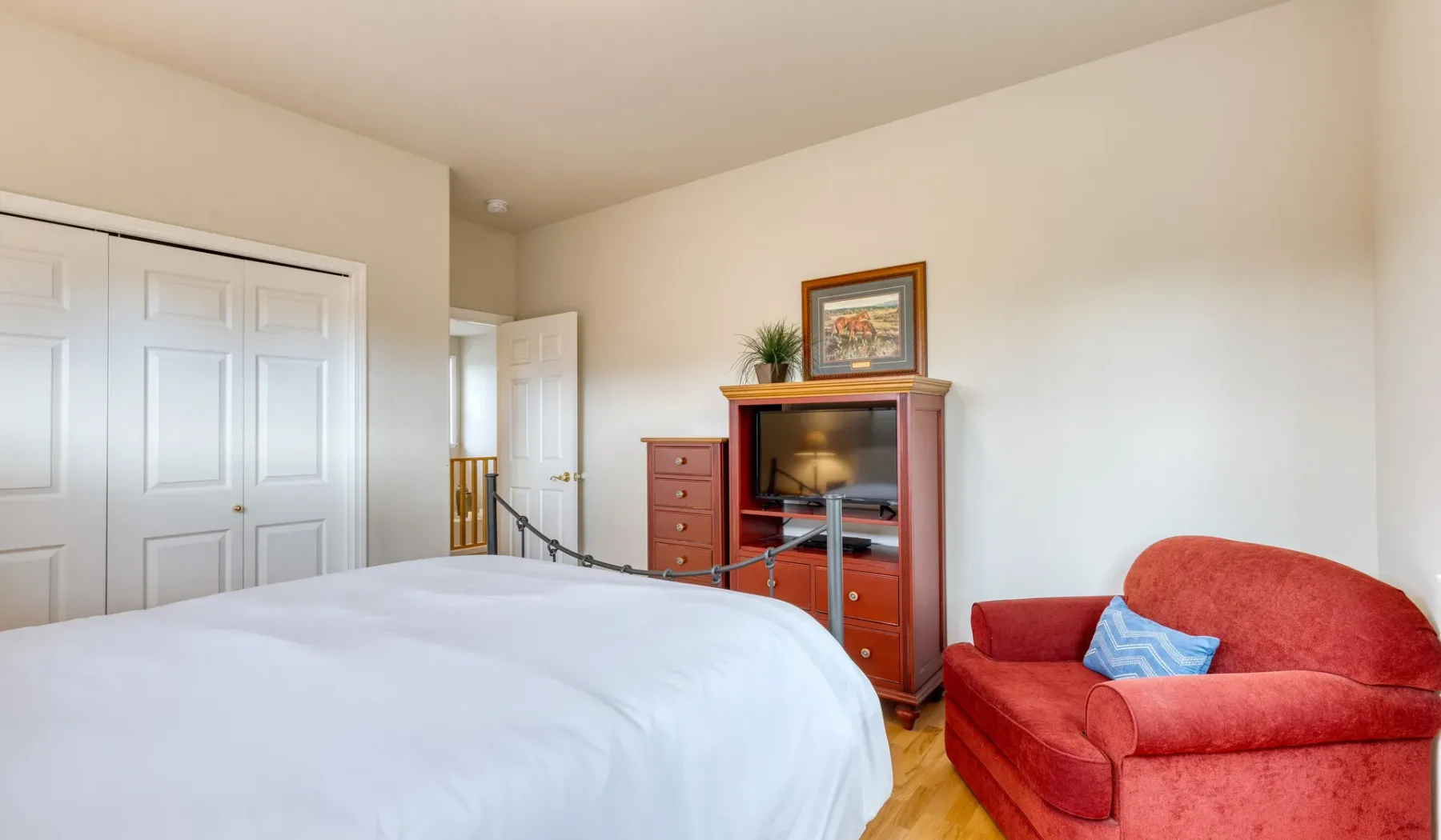 A bedroom with a bed, wooden dresser, and red upholstered seating.