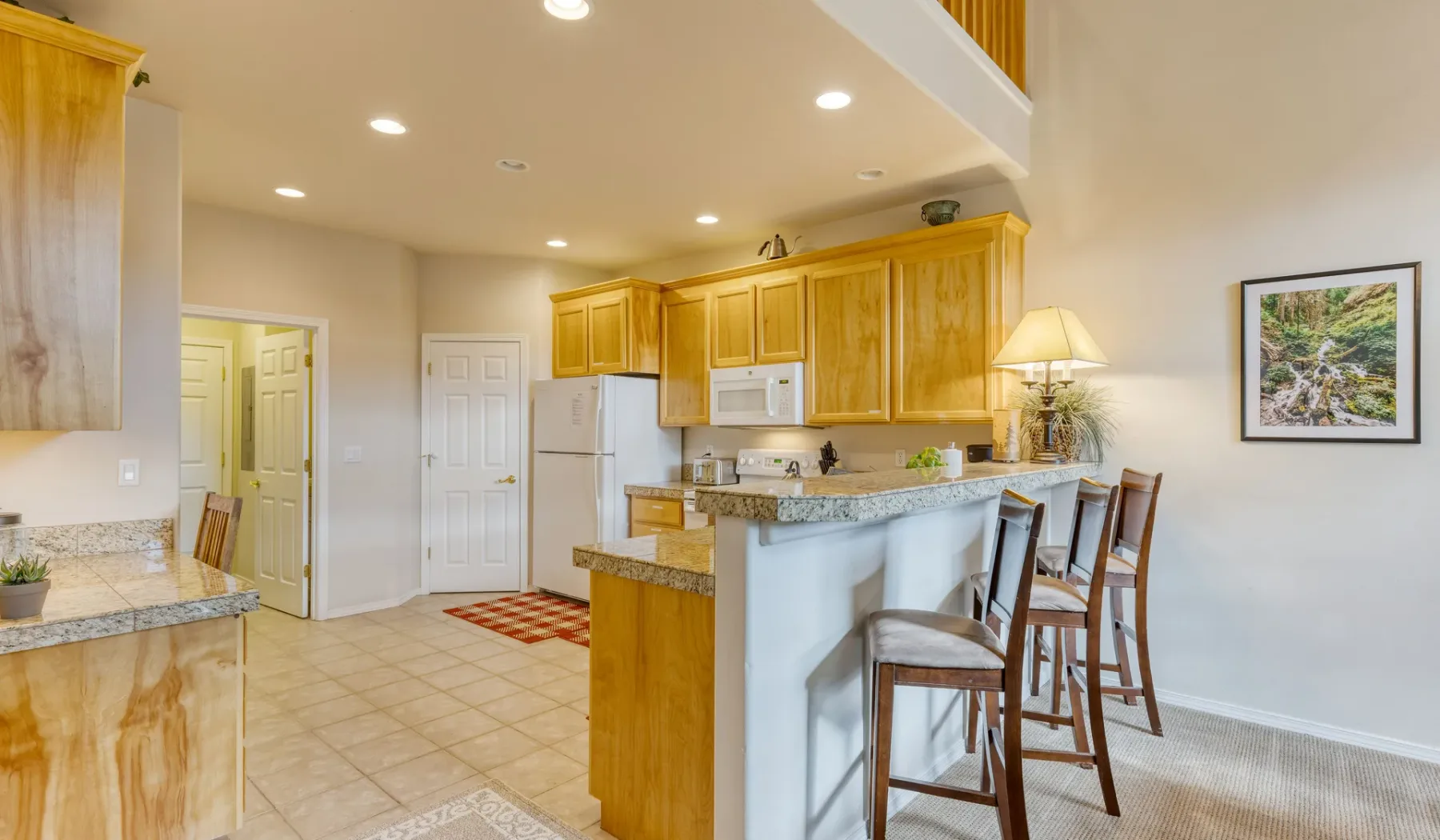 A bright kitchen with wooden cabinets and a breakfast bar with stools.