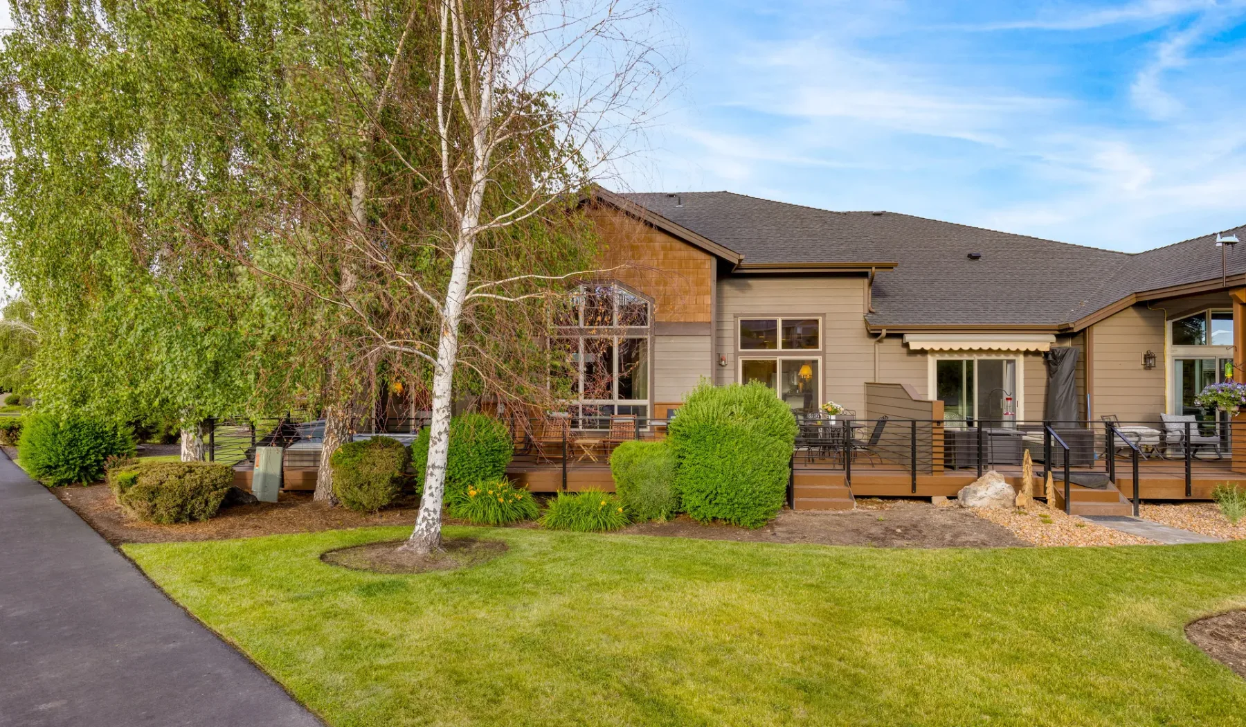 A landscaped house exterior with a lawn, shrubs, and a paved path.