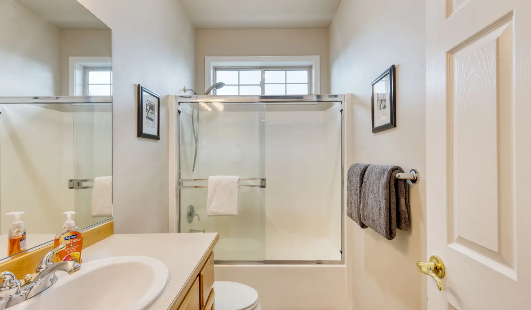 A bright bathroom with a sink, mirror, and glass shower.