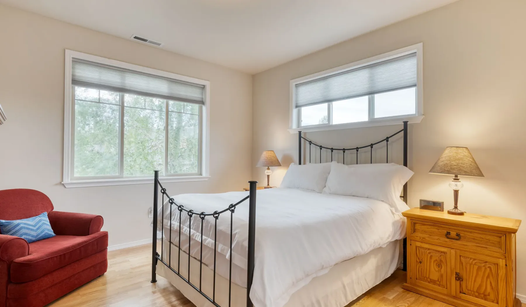 A bedroom with a white bed, windows, and a red armchair.