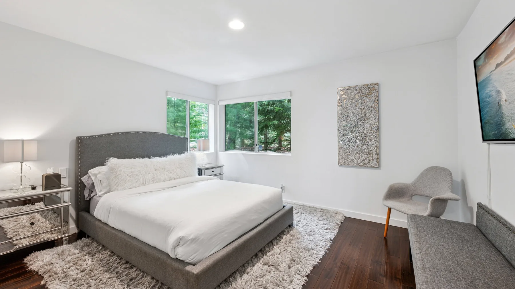 Un dormitorio luminoso con una cama tendida, ventanas amplias y una zona de estar.