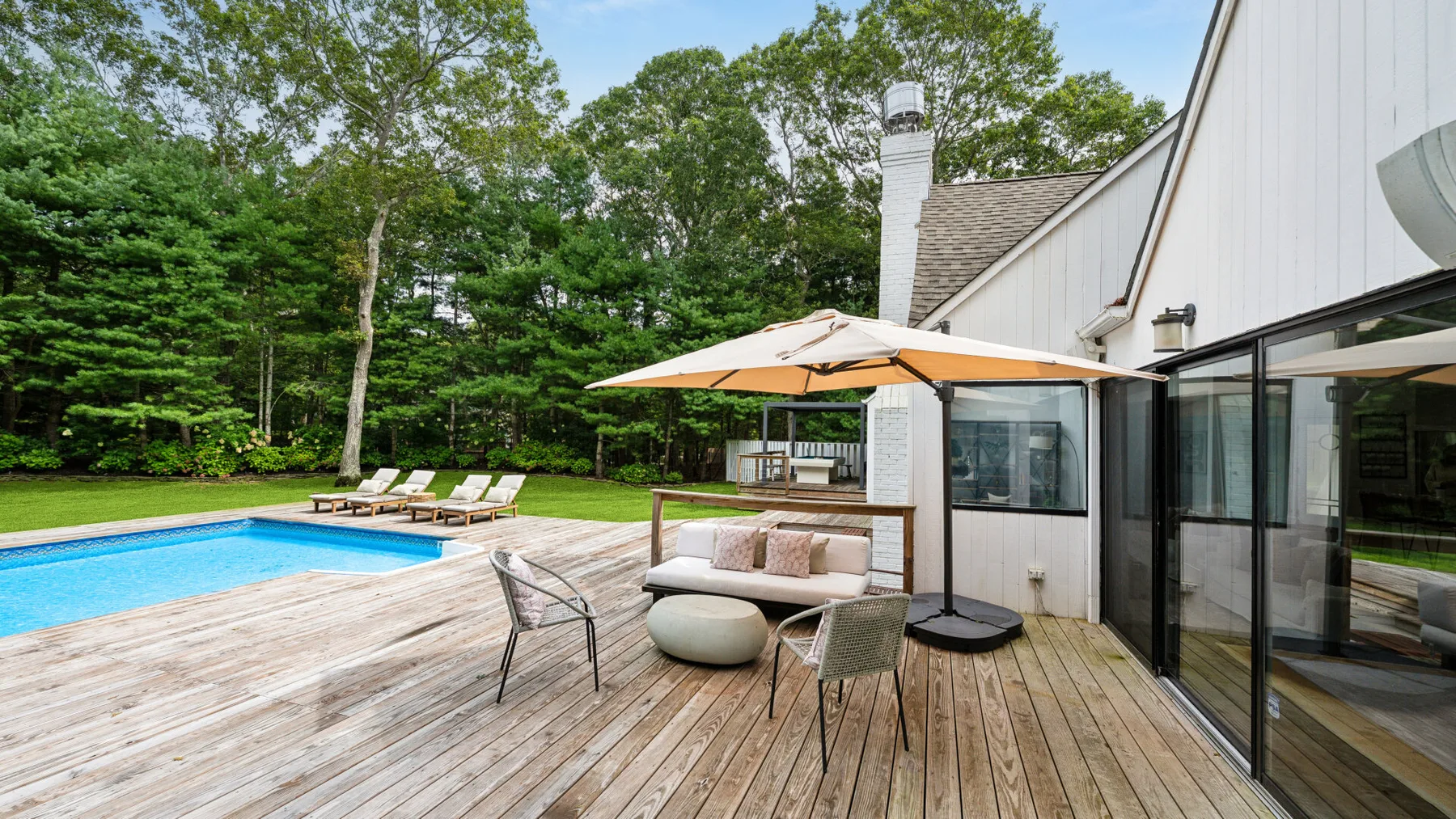 Una piscina en el patio junto a una terraza de madera, asientos al aire libre y una casa.