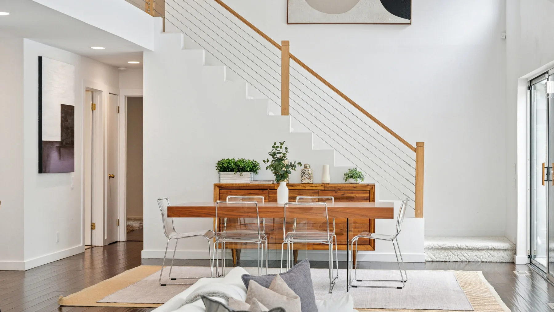 Un comedor luminoso con una mesa de madera bajo una escalera.