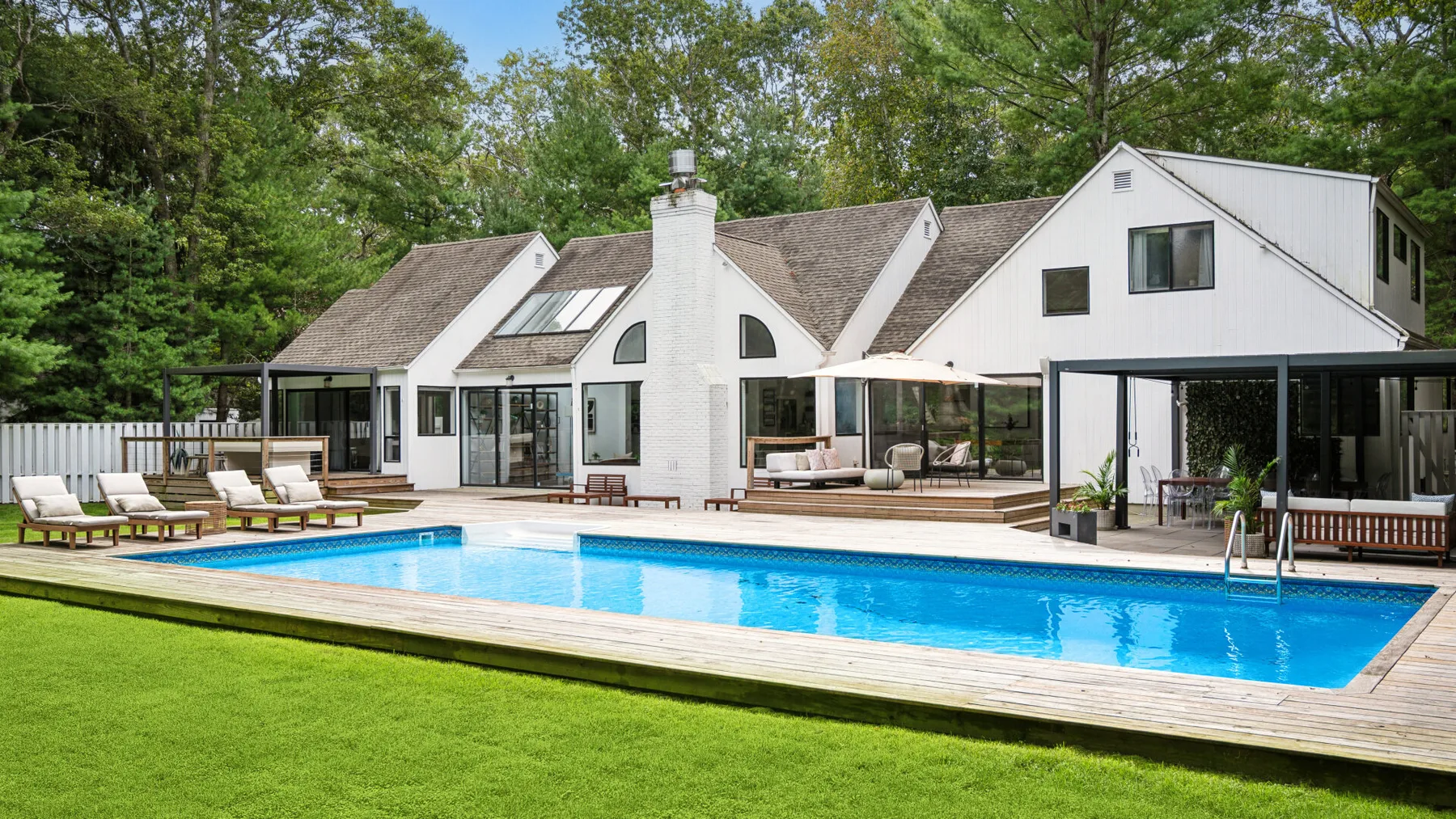 Una casa blanca da a una piscina y un césped verde.