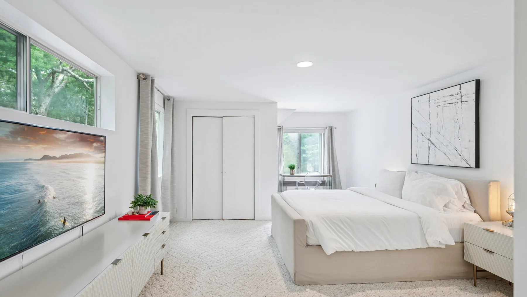 Un dormitorio luminoso con una cama, mesitas de noche y un televisor montado en la pared.