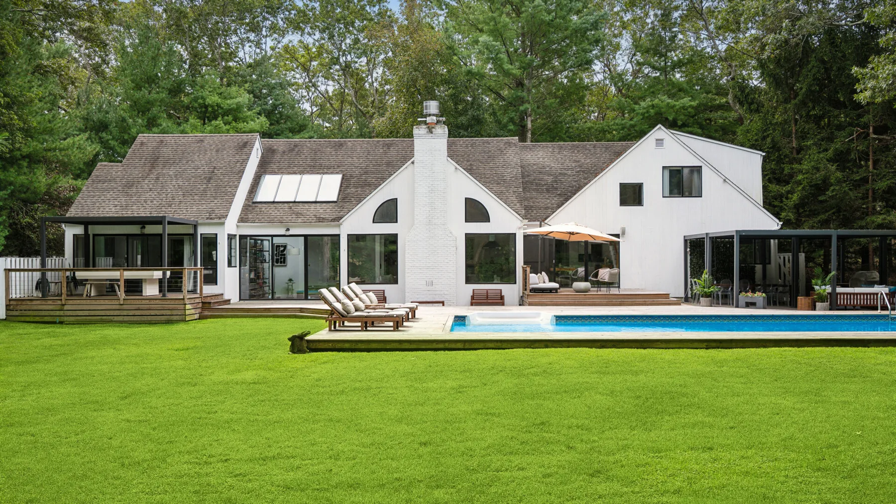 Una casa blanca se alza tras un amplio césped verde, con una piscina delante.