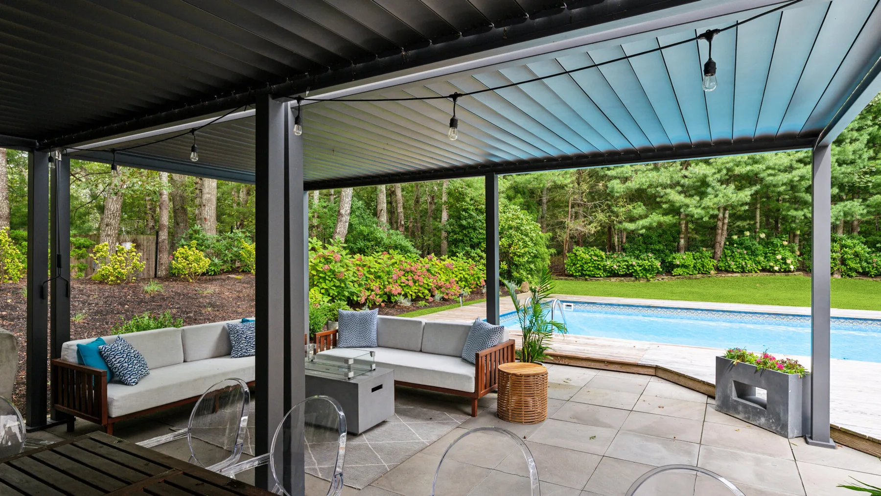 Un patio cubierto con asientos al aire libre da a una piscina y un jardín.