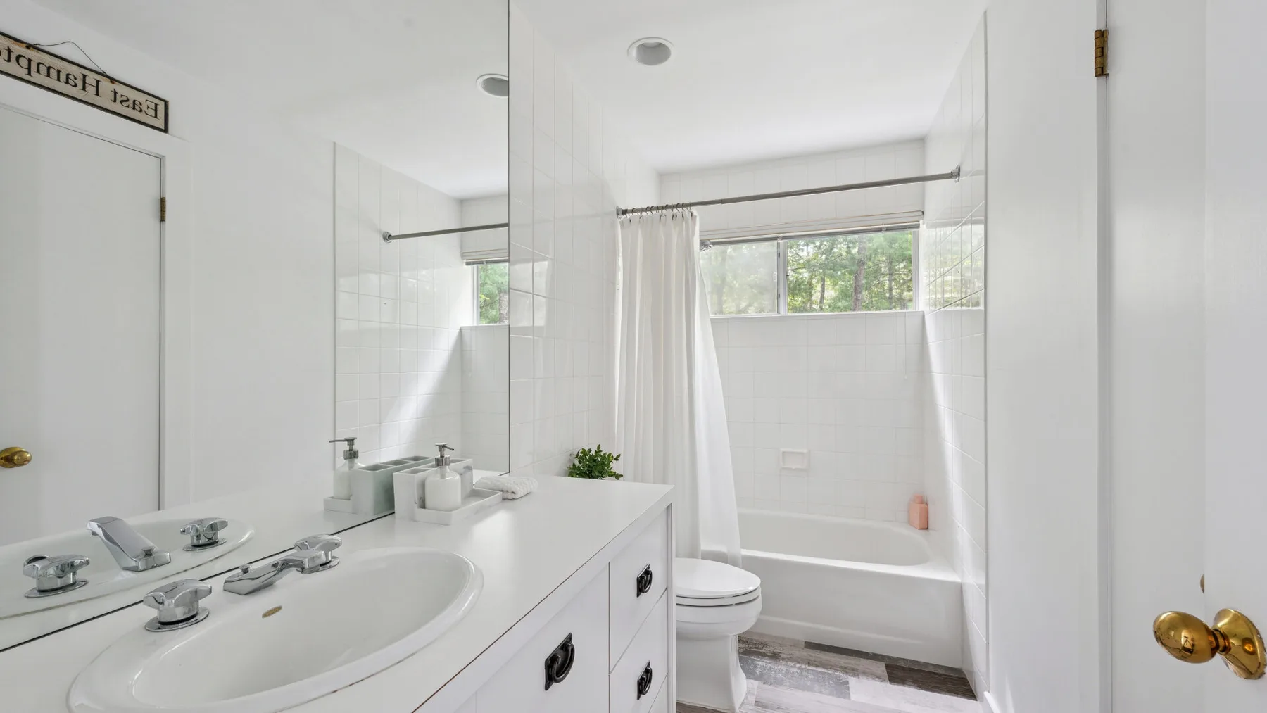 Un baño luminoso con una larga encimera de lavabo y una bañera detrás de una cortina.