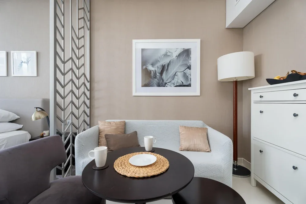 A sitting area with a light-colored loveseat, round table, and floor lamp.