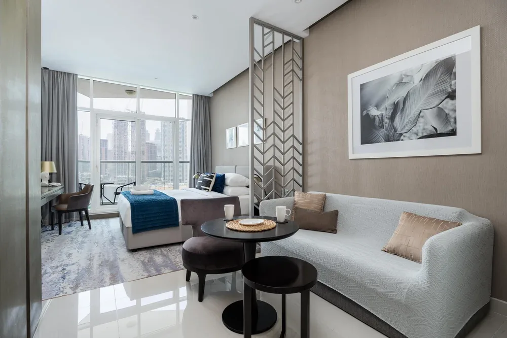 A bright living area has a light-colored sofa, round tables, and large windows.