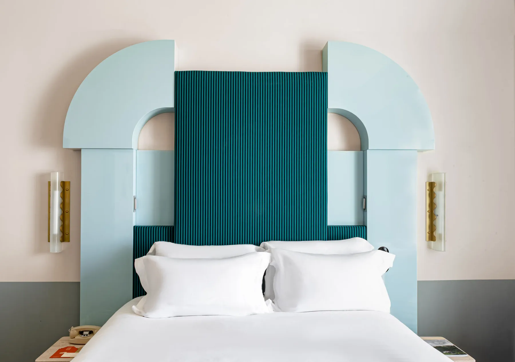 Habitación con cabecero tapizado en verde esmeralda y ropa de cama blanca.
