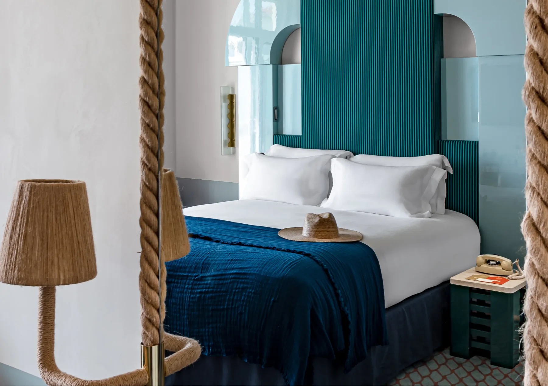 Cama con dosel, cabecero verde azulado y manta decorativa azul.