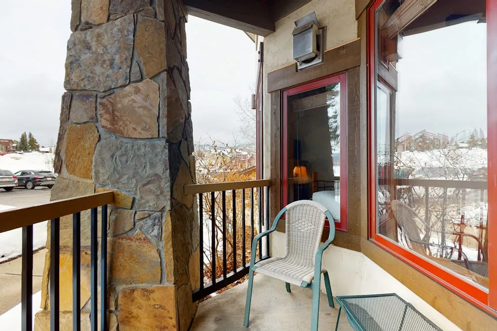 A covered balcony with a chair and windows overlooking a snowy landscape.