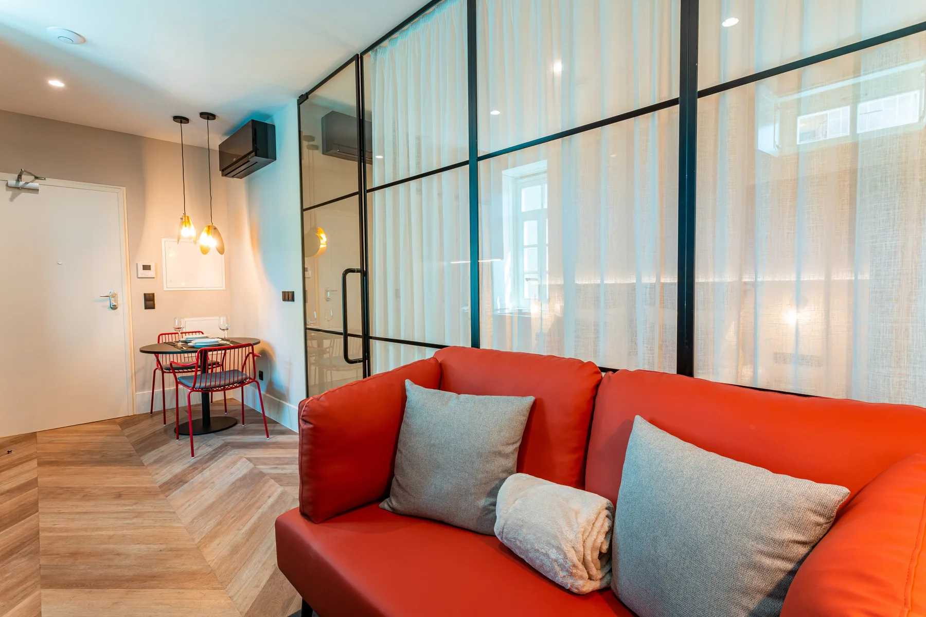 A living area with red seating beside a glass partition and dining table.