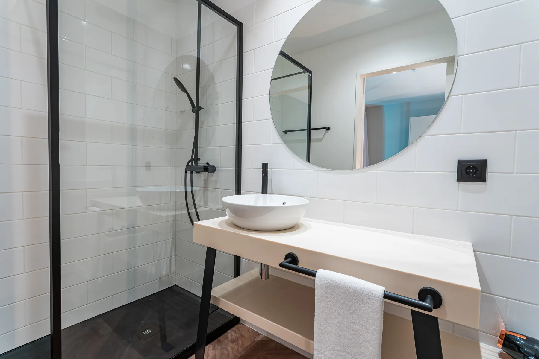A modern bathroom with a glass shower and a round mirror above the sink.
