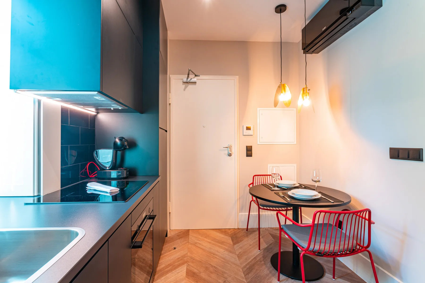 A compact kitchen and dining area with a table and red seating.
