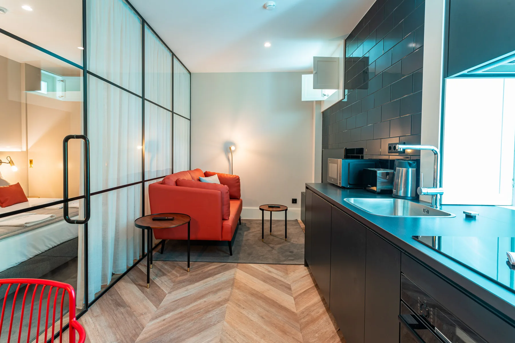 An open-plan apartment interior with red seating beside a compact kitchen.