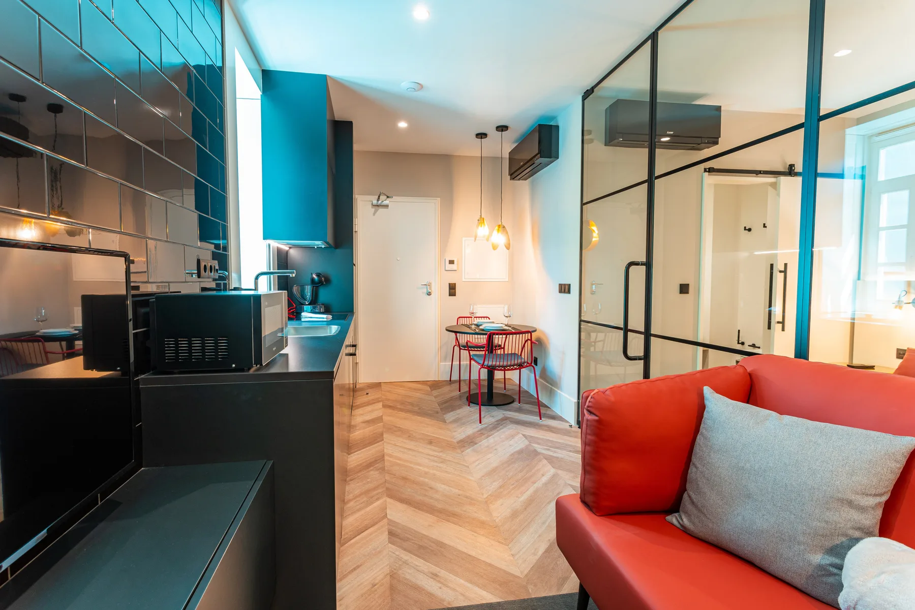 A modern apartment living area with a red sofa, dining table, and kitchen.
