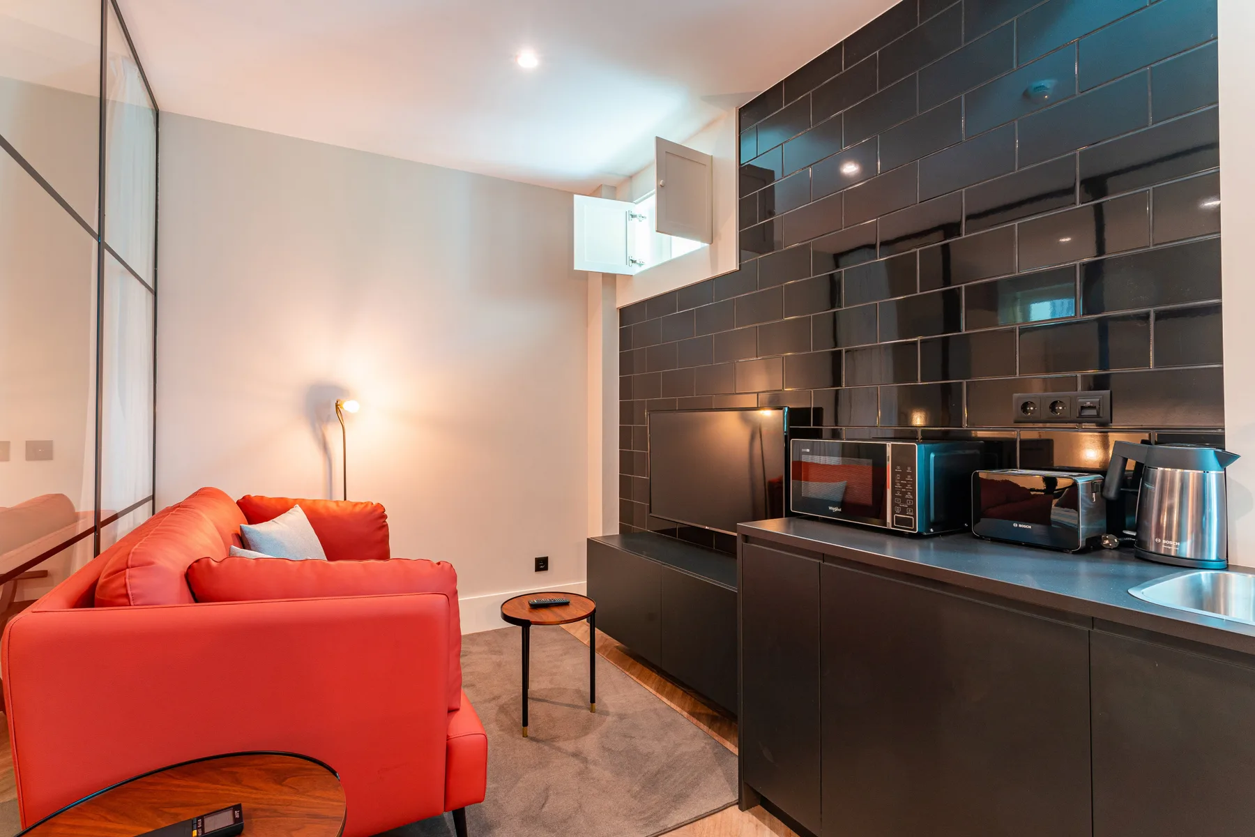 A modern living area with red seating beside a compact kitchen.