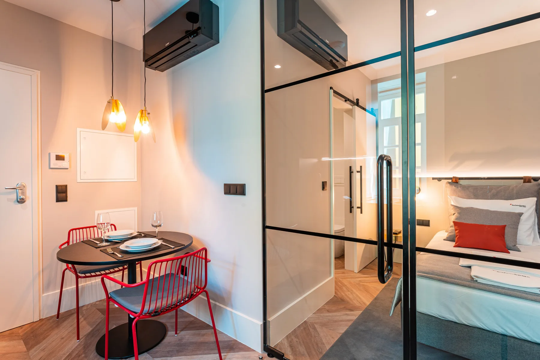 A bedroom with a bed beside a glass partition and a small dining table.