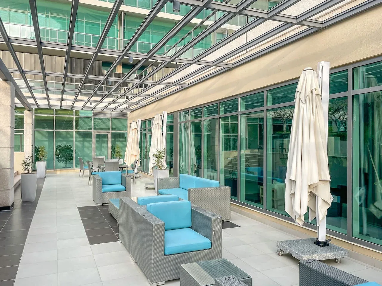 Un salón exterior cubierto con asientos de cojines azules junto a grandes ventanales.