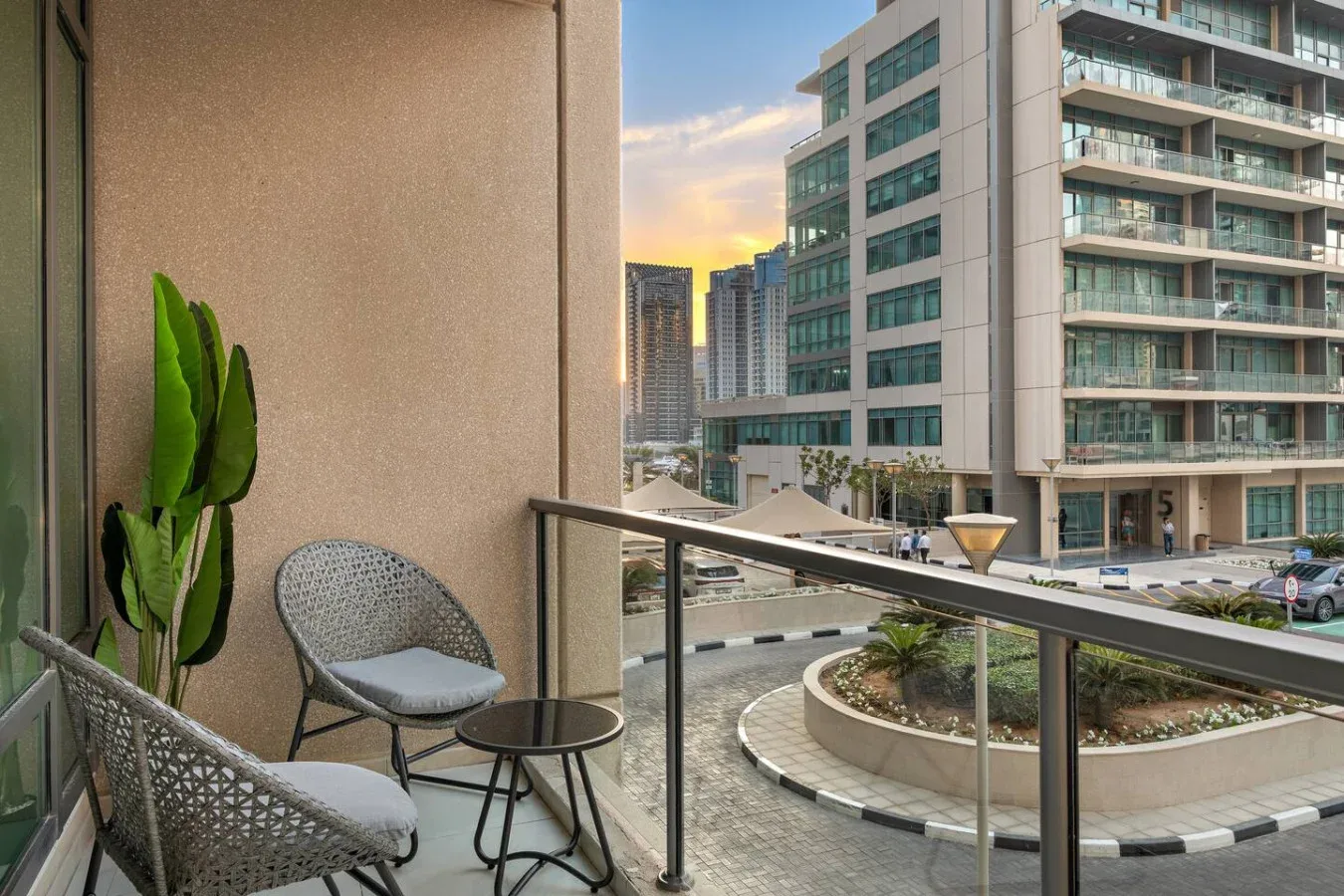 Una zona de estar en el balcón da a un patio ajardinado y edificios modernos cercanos.