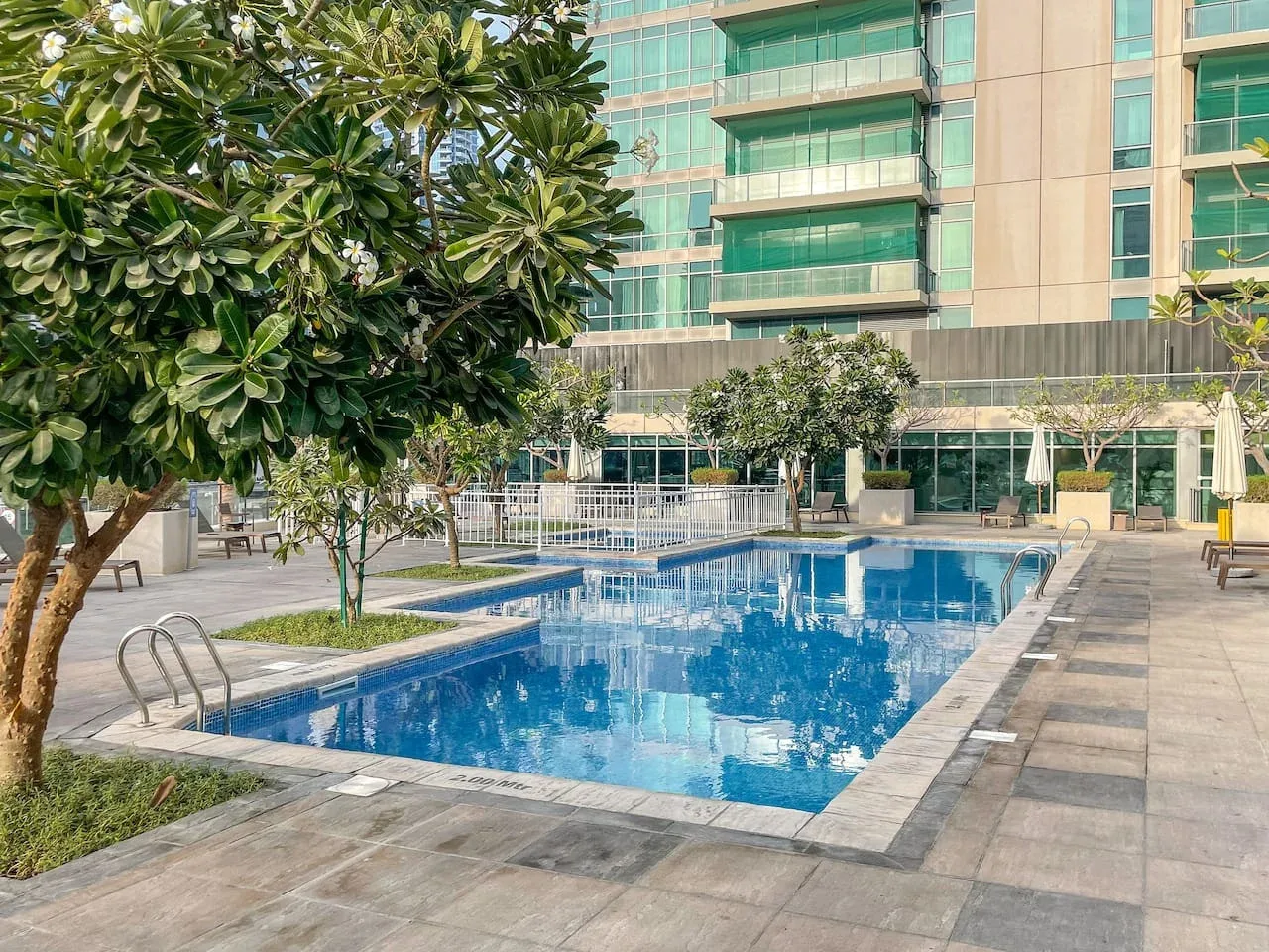 Una piscina al aire libre está junto a un edificio moderno y árboles.