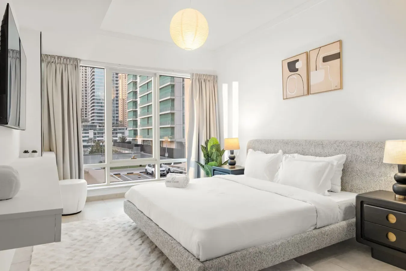 Un dormitorio luminoso con una cama grande, mesitas de noche y vistas de la ciudad por la ventana.