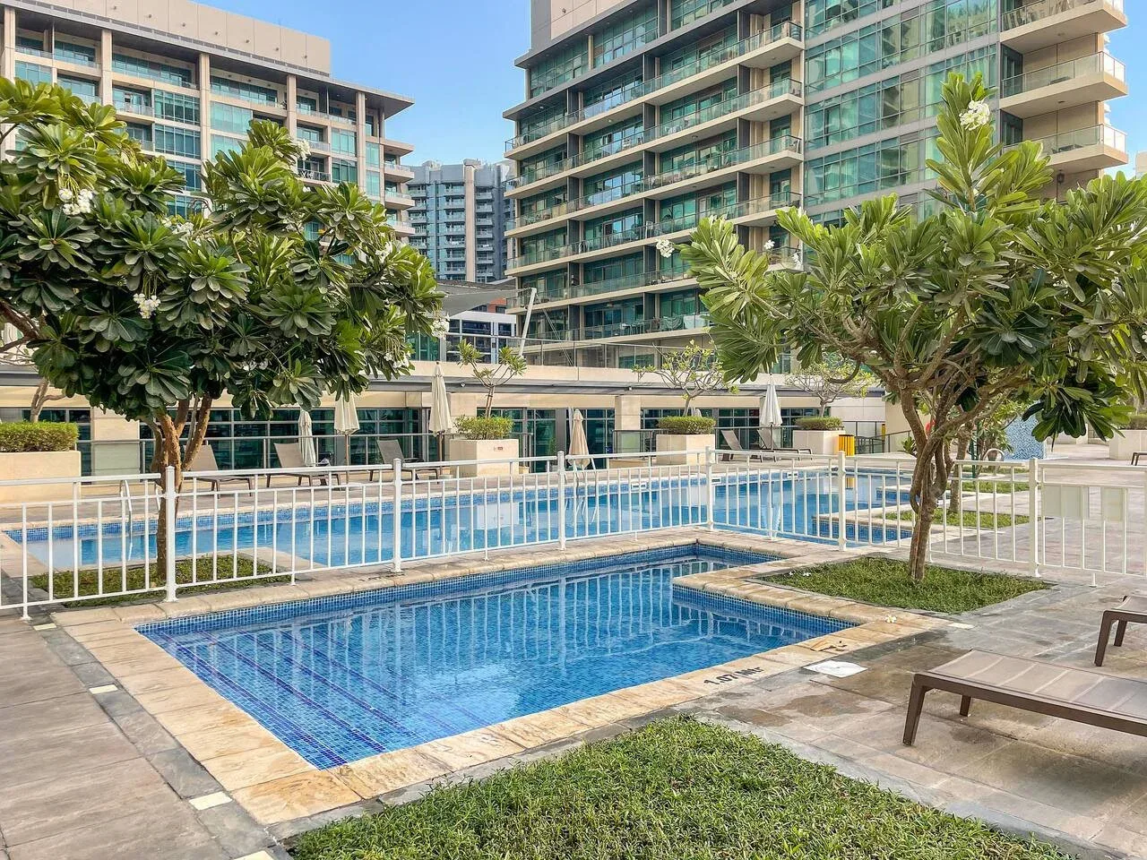 Una piscina al aire libre está rodeada de árboles y edificios de apartamentos modernos.