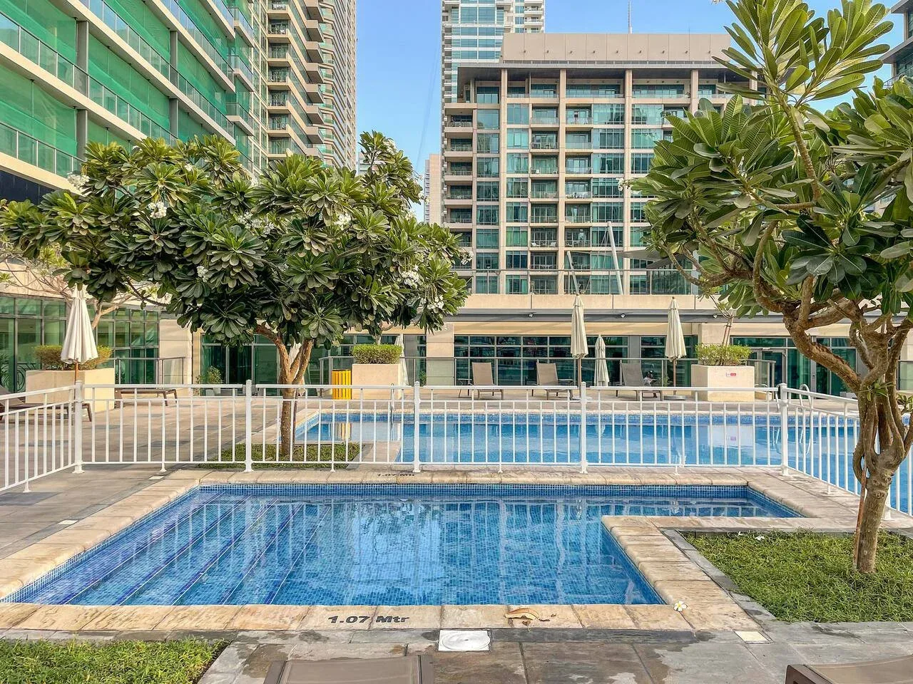 Una piscina al aire libre está rodeada de árboles y edificios modernos de gran altura.
