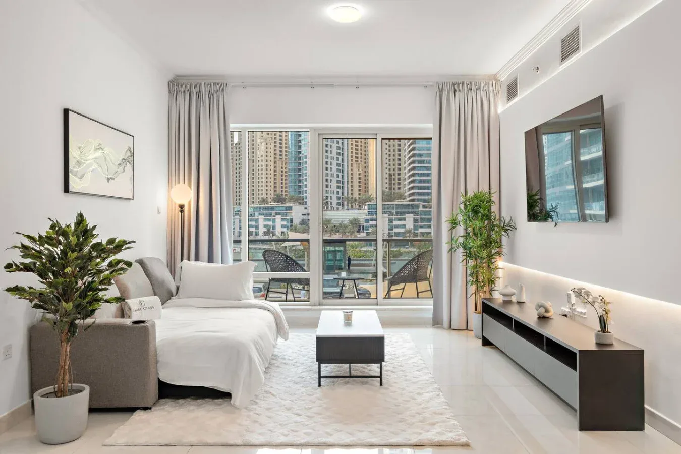Una sala luminosa con asientos, una mesa de centro y grandes ventanas con edificios a la vista.